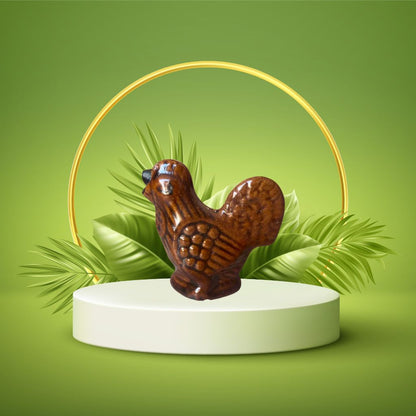A brown miniature figurine of a hen presented on a white pedestal with a green background and decorative leaves.